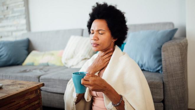 Mulher enroladaea sports fc 23cobertor segurando xícaraea sports fc 23chá e com a mão na garganta