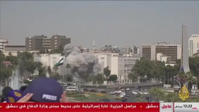 生放送中に背後で空爆が起き、身をかがめる記者