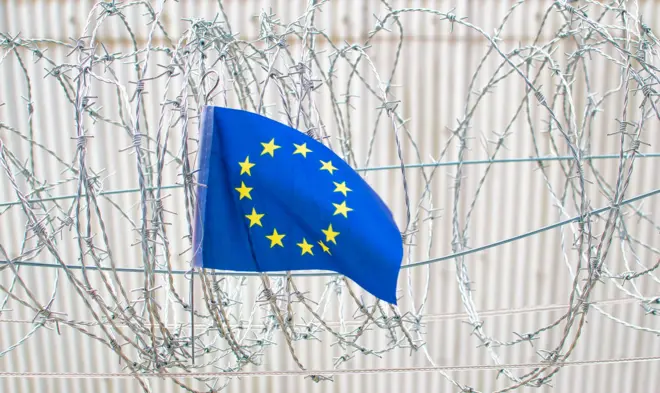 Bandera de la UE frente a una valla con alambre de púas