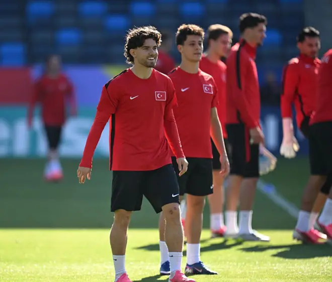 Ferdi Kadıoğlu sahada gülümsüyor. Arkasında bir dizi Türk milli futbolcu var