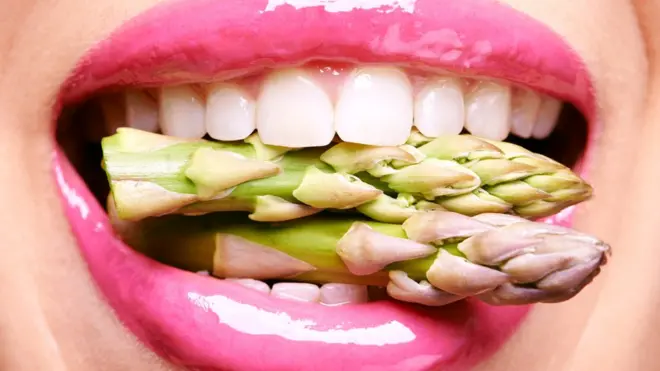 Una boca con espárragos crudos.