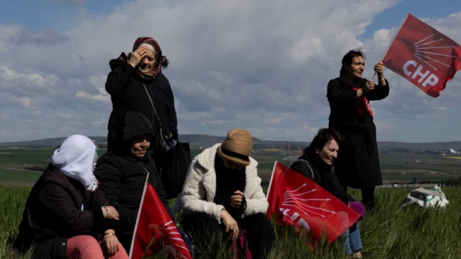 Beş CHP'li kadın ellerinde parti bayraklarıyla çim alanda oturuyor. Hava rüzgarlı ve soğuk görünüyor