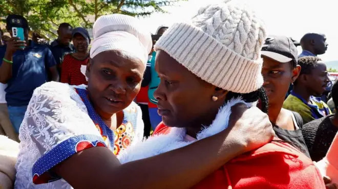Two women, one in a white headscarf and the other in a beanie hat embracing