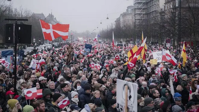 Büyük bir cadde binlerce kişi var. Ellerinde Grönland'ın ve Danimarka'nın kırmızı beyaz bayrakları var.