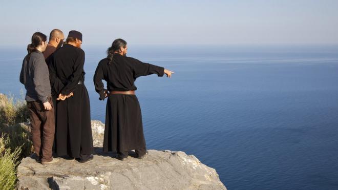 Monges e peregrinos observam a vista de Monte Athos, na Grécia