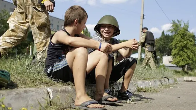 Війна стала вимушеним фоном і сьогоденням для багатьох українських дітей. Обстріли нищили школи і дитячі майданчики, гинули рідні і друзі. На фото - діти і український військовий у місті Попасна, серпень 2014-го року