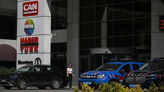 Bir binanın girişinde Can Holding, Show Tv ve Haberturk logosu, arabalar, güneş gözlüklü bir kadın