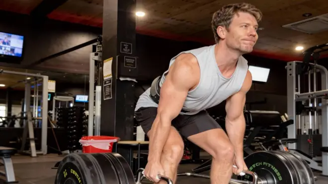 Dr Michael lifting weights at the gym in a grey singlet