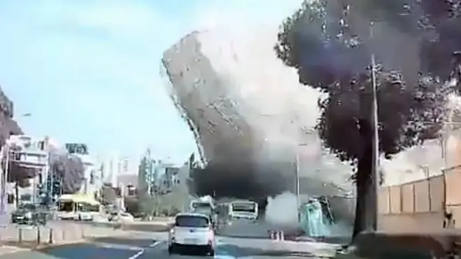 철거 공사 중이던 5층 건물이 도로 쪽으로 무너지며 지나가던 시내버스를 덮치고 있다