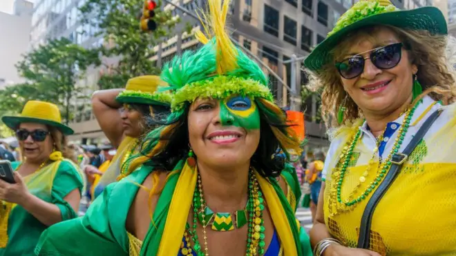 Duas brasileiras durante o evento Brazilian Day em Nova York, em 2016. Elas vestem roupas verdes e amarelas e uma delas tem o rosto parcialmente pintado com a bandeira brasileira