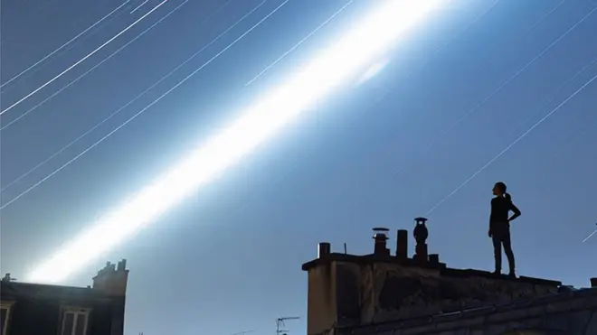 An image showing a woman standing on a Parisian rooftop with a long exposure view of the night sky