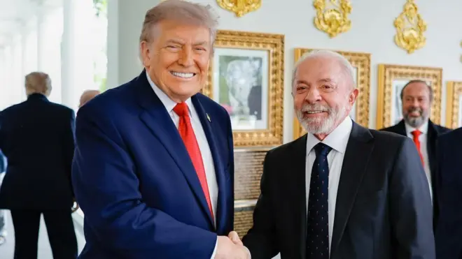 Trump e Lula olhando para a foto enquanto sorriem e apertam as mãos 