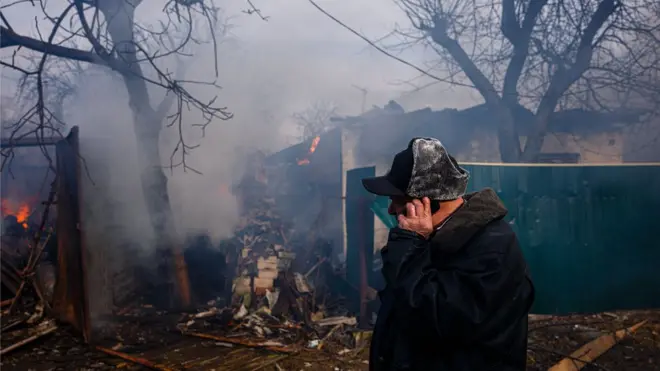 A man talks on a phone in front of his burning house damaged after shelling in the city of Chernihiv on 4 March 2022.