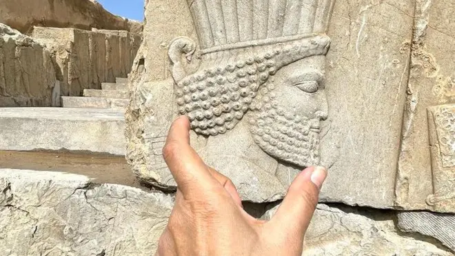 Una mano muestra el perfil de un rostro esculpido en una pared de piedra