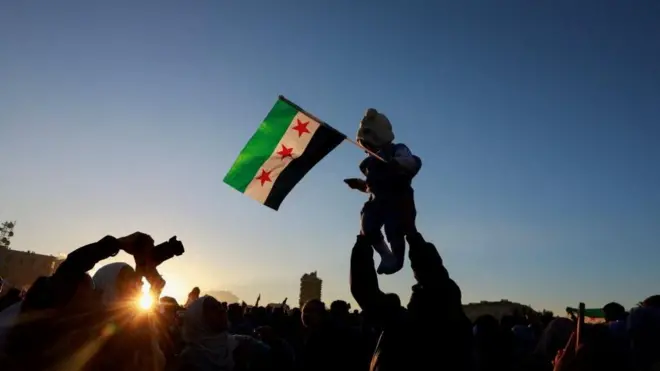 حشود سورية تحتفل بسقوط حكم الأسد حيث يظهر في الصورة طفل يحمل على سوريا الذي تبناه معارضو الأسد