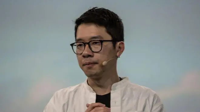 短髪でめがねをかけた男性の写真。顔の左側にインカムをつけている。