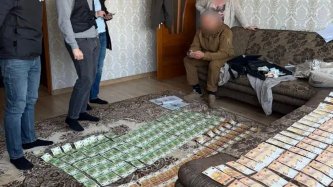 Людина з заблюреним обличчям сидить перед розкладеними грошима 