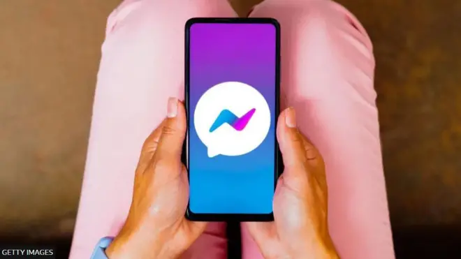 امرأة تحمل جهاز هاتف خلوي يظهر عليه تطبيق ماسنجر 