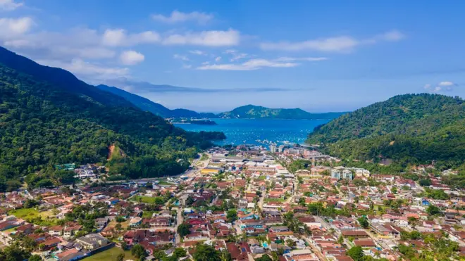 Vista aérea da praia do Lázaro, em Ubatuba, com adensamento urbano entre montanhas e o mar ao fundo