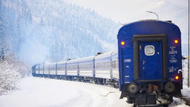 Синій потяг їде крізь сніг на фоні гори