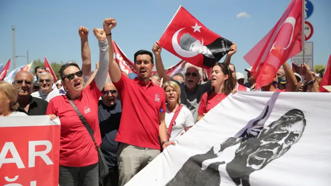İzmir mitinginde Özgür Özel pankartı ve Atatürk ve Türk bayrakları taşıyan kitleden bazıları yumrukları yukarıda slogan atıyor
