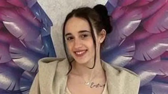 Joana stood against a wall with multi-coloured rainbow wings painted on