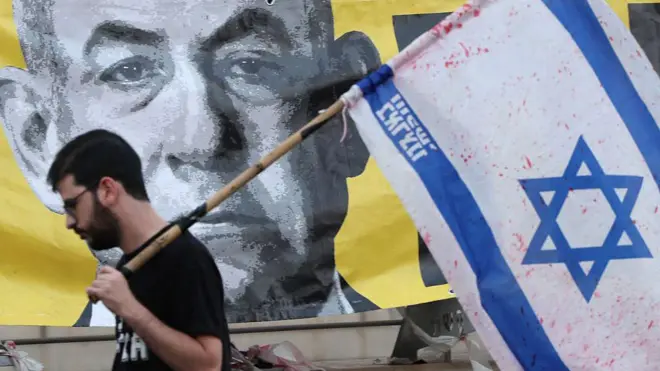 Un hombre con una bandera israelí pasa delante de una imagen de Netanyahu.
