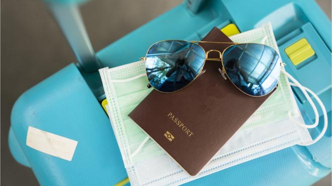 Passaporte, óculos escuros, máscara e mala