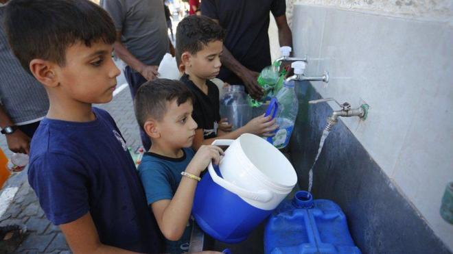 Los niños llenan cajas con agua limpia de un dispensador mientras ocurre la escasez de agua en Deir-Al Balah, Gaza.