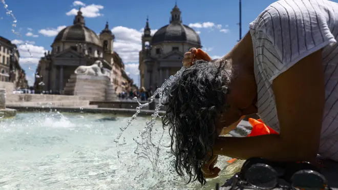 Женщина окунает голову в фонтан на фоне собора