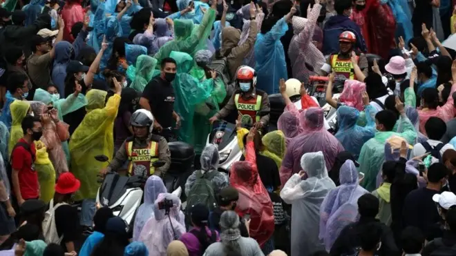 Pro-democracy protesters show the three-finger salute as police officers drive by during an anti-government protest, in Bangkok, Thailand October 17, 2020