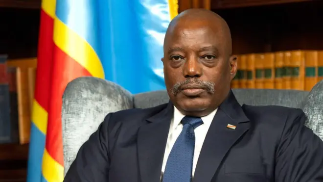 Joseph Kabila wahoze ari perezida wa DR Congo yicaye mu ntebe yambaye isuti y'umukara inyuma ya hari ibendera rya RD Congo