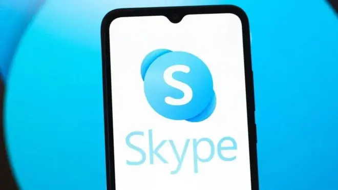 Стоковая картинка. На голубом фоне телефон, в котором на белом фоне написано Skype и виден логотип приложения.