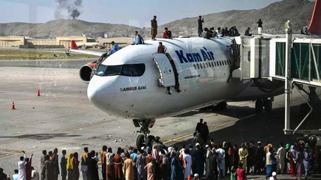 People clamber on top of planes as smoke rises in the distance