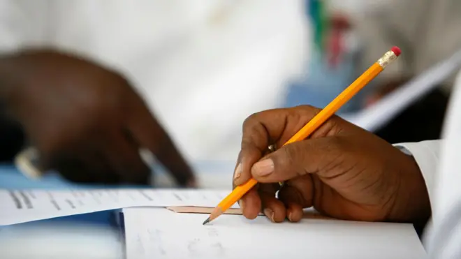 A student writing with pencil while another reads