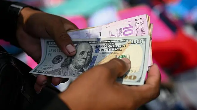 Un hombre sujeta unos billetes de dólares y bolívares.