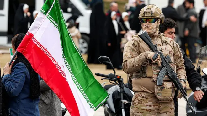 Un efectivo de la Guardia Revolucionaria en Teherán sostiene un fusil automático junto a una mujer que porta una bandera de Irán