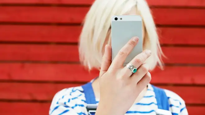 Perempuan memegang ponsel pintar di depan mukanya