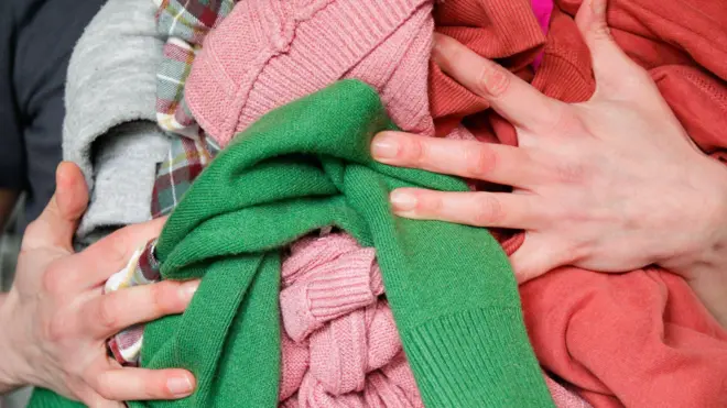 Mãos de uma pessoa segurando várias peças de roupas