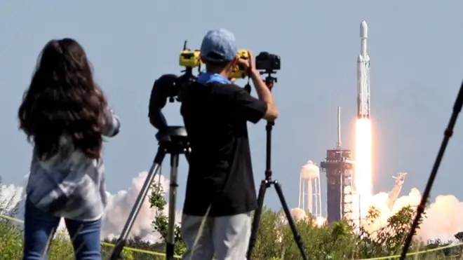 Two spectators look on as a SpaceX Falcon Heavy rocket with the Europa Clipper spacecraft aboard launches from Launch Complex 39A at NASA's Kennedy Space Center in Cape Canaveral on 14 October 2024.