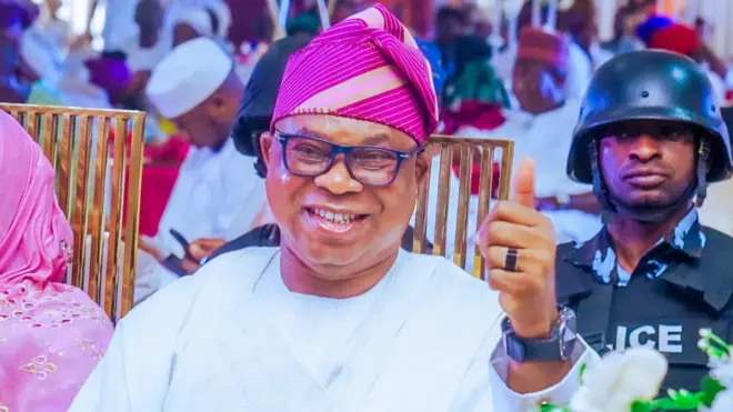 Bọla Oyebamiji wa nibi apero kan to si na ọwọ osi soke, ọlọpaa kan wa lẹyin rẹ.