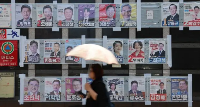 벽보 앞을 지나는 우산을 든 여성