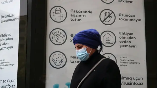 Üzü maskalı qadın koronavirus lövhəsi qarşısında