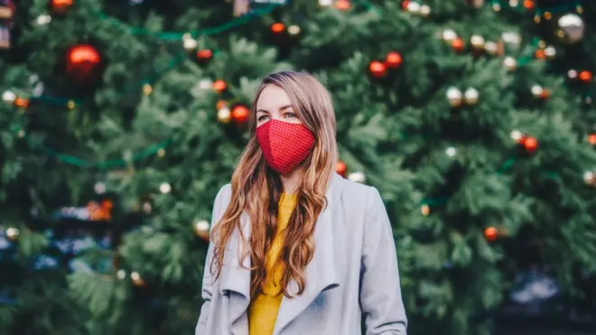 Women in face mask in front of Christmas tree