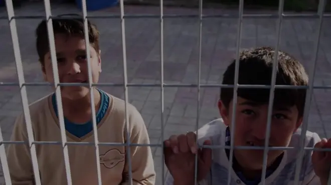 Children looking through a wire fence at the camera