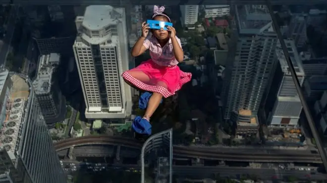 A girl observes a partial solar eclipse on the Mahanakhon Skywalk Glass Tray at the King Power Mahanakhon building in Bangkok, Thailand.