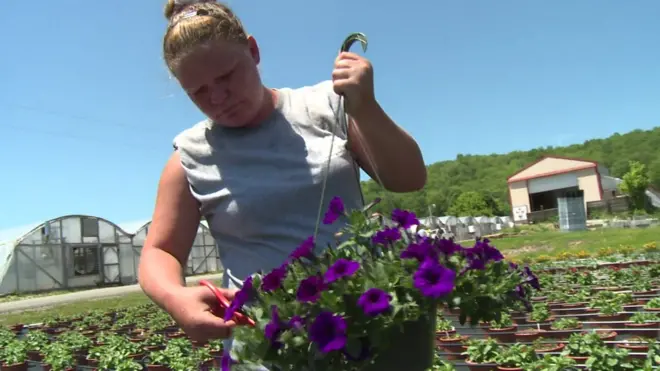 Una mujer arregla un tiesto con flores.