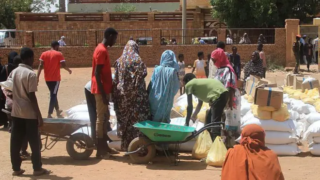مواطنة سودانية تنظر، بينما يحاول عدد من المواطنين السودانيين تجميع بعض المساعدات الإنسانية.