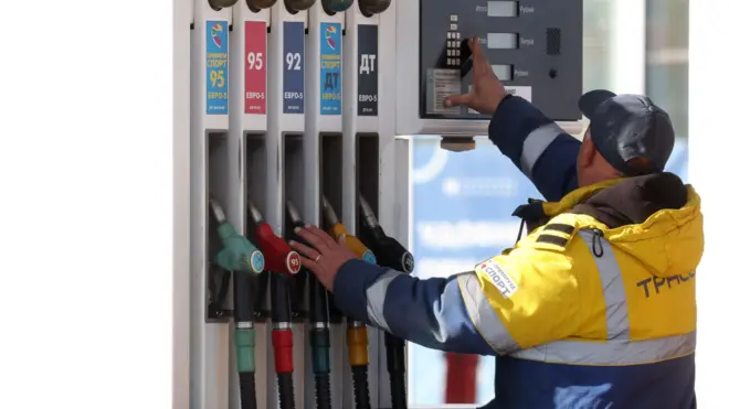 Співробітник АЗС у Москві в жовтій фірмовій куртці зі світловідбивними смужками стоїть біля кранів із бензином спиною до об'єктива