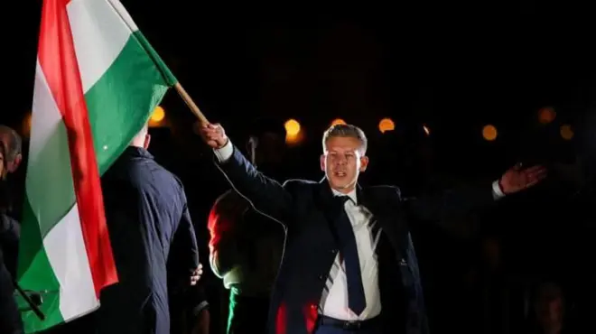 Peter Magyar, con los brazos abiertos y una bandera húngara, celebra su victoria en Budapest.